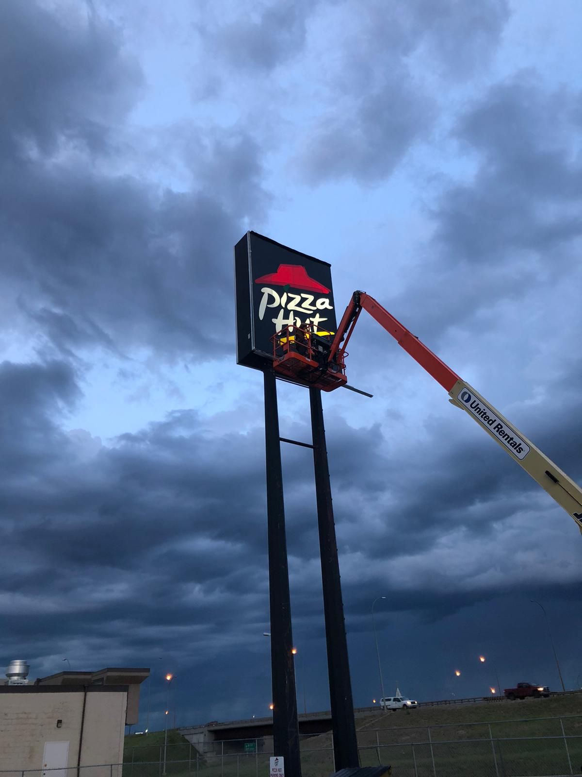 Pizza Hut illuminated freestanding pylon sign being installed at dusk